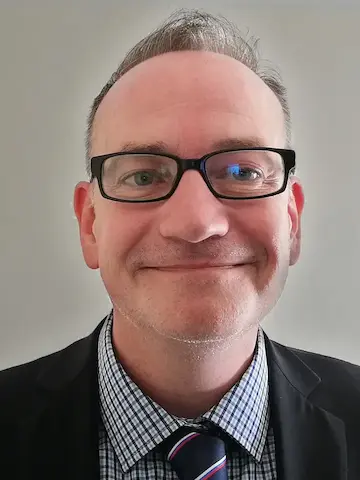 A portrait of a smiling man wearing glasses and a natty suit.